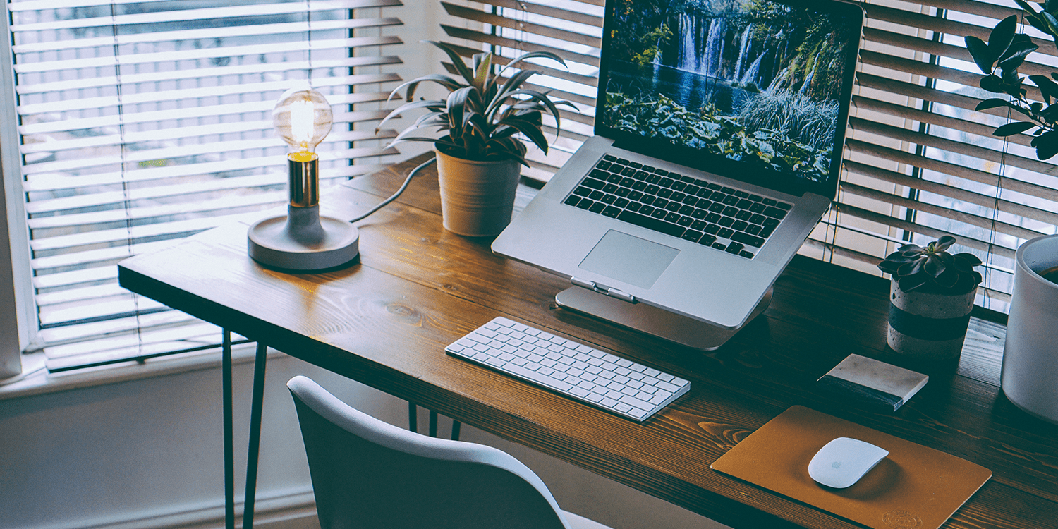 Image of a small home office containing a wooden desk with a laptop, keyboard, and other desk accessories, illustrating the concept of using a home address as a registered office