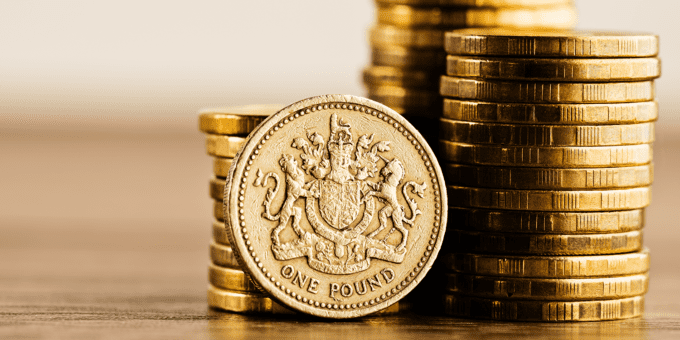 Stacks of pound coins on a wooden desktop.