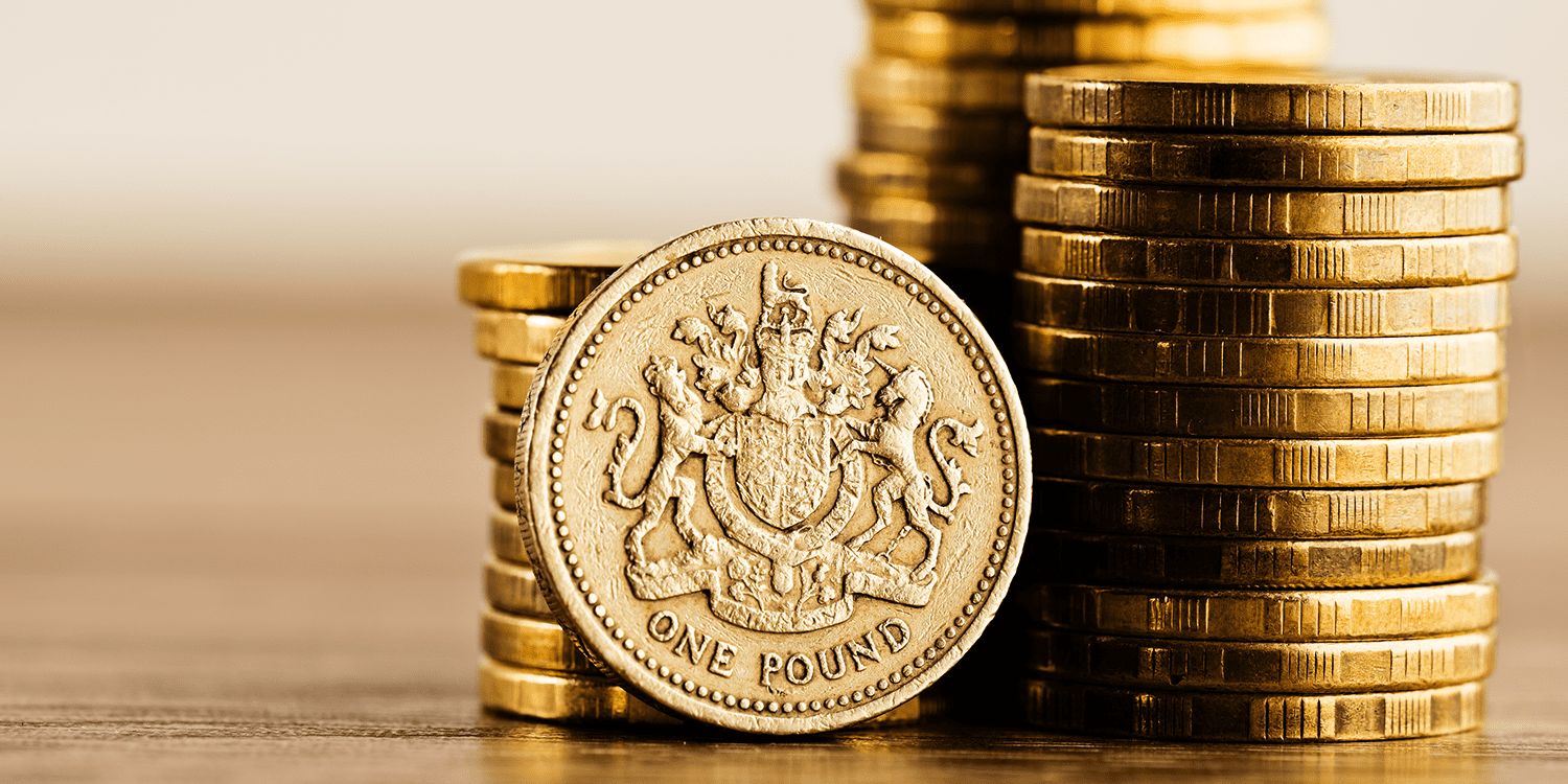 Stacks of pound coins on a wooden desktop.