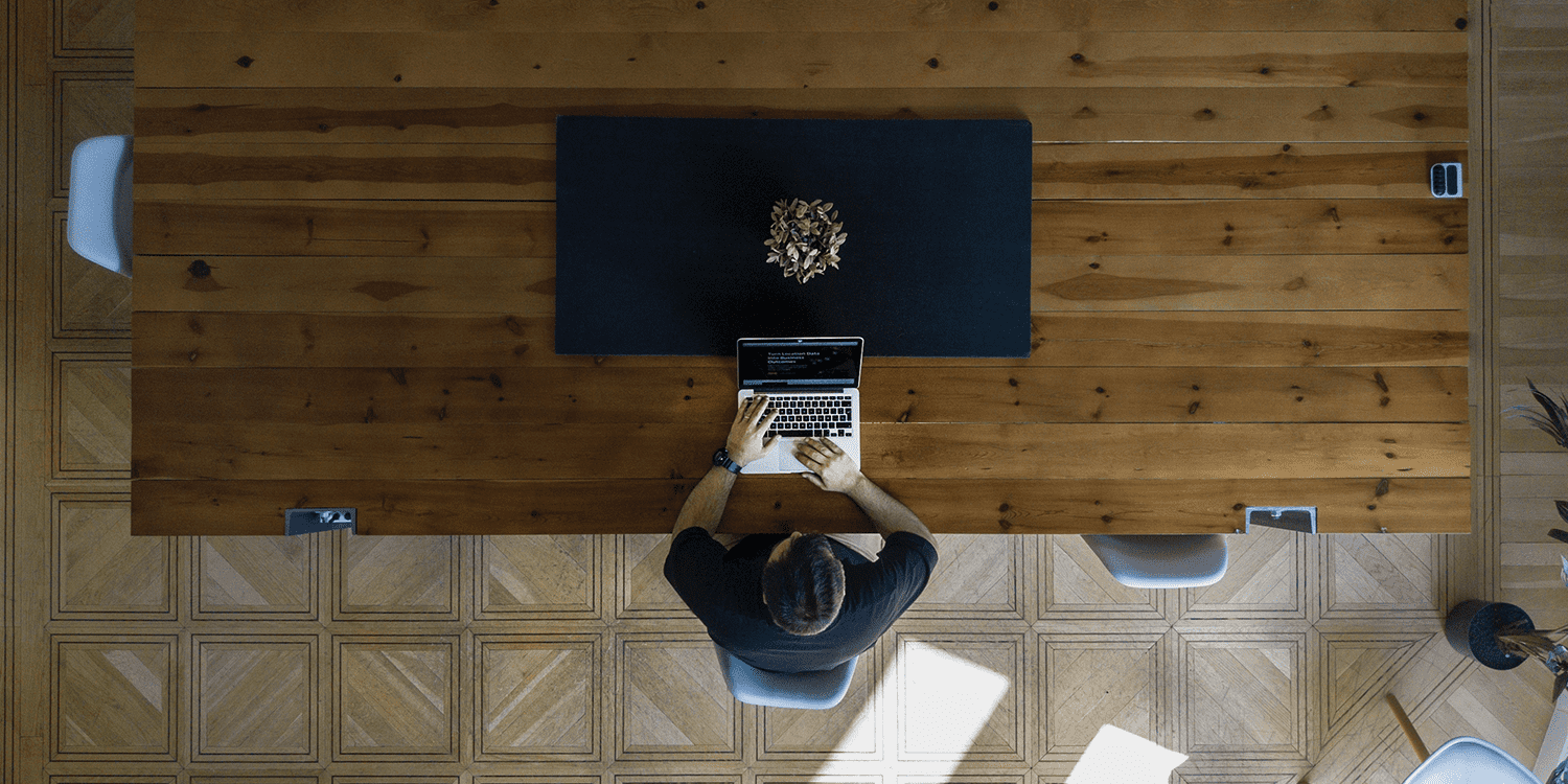 Bird's eye view of a person sitting at a table whilst typing on a laptop, illustrating that you only require one person to form a limited company.