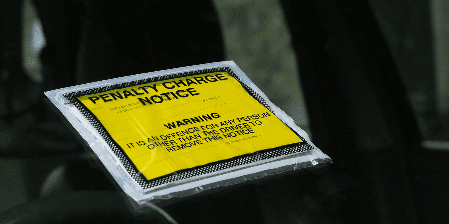 A square, yellow Penalty Charge Notice stuck to the windshield of a car, illustrating the concept of late filing penalties imposed on limited companies.