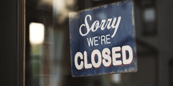 A sign hanging from a glass-fronted door, displaying the words "Sorry, we're closed".
