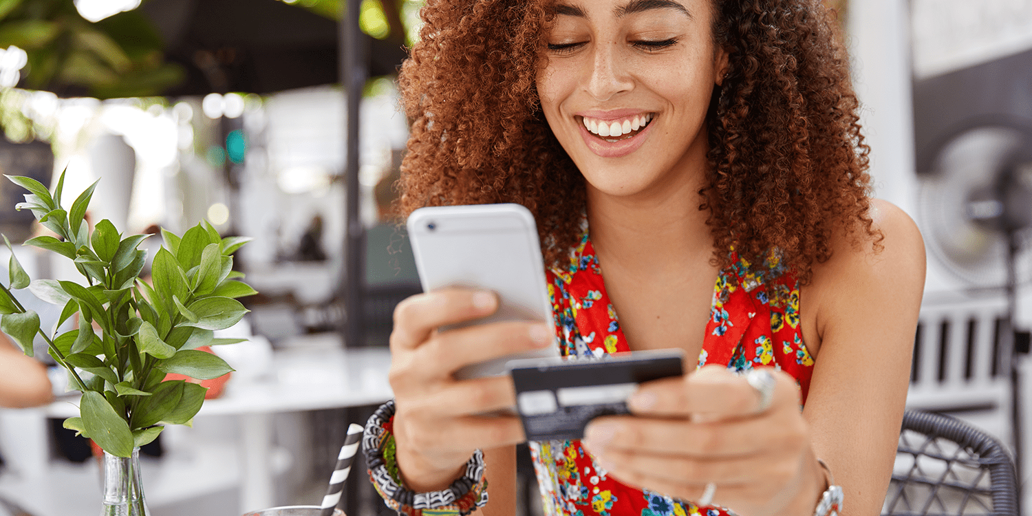 Image of a woman holding a mobile phone in one hand and a bank card in the other, illustrating the process of managing a business bank account online.