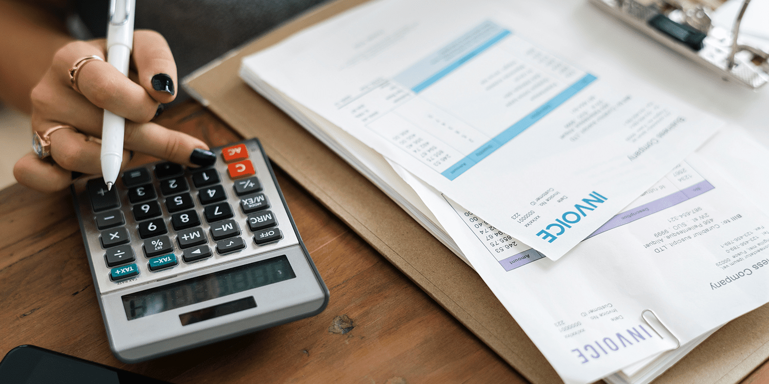 A business person processing supplier invoices with a desktop calculator and pen in hand.