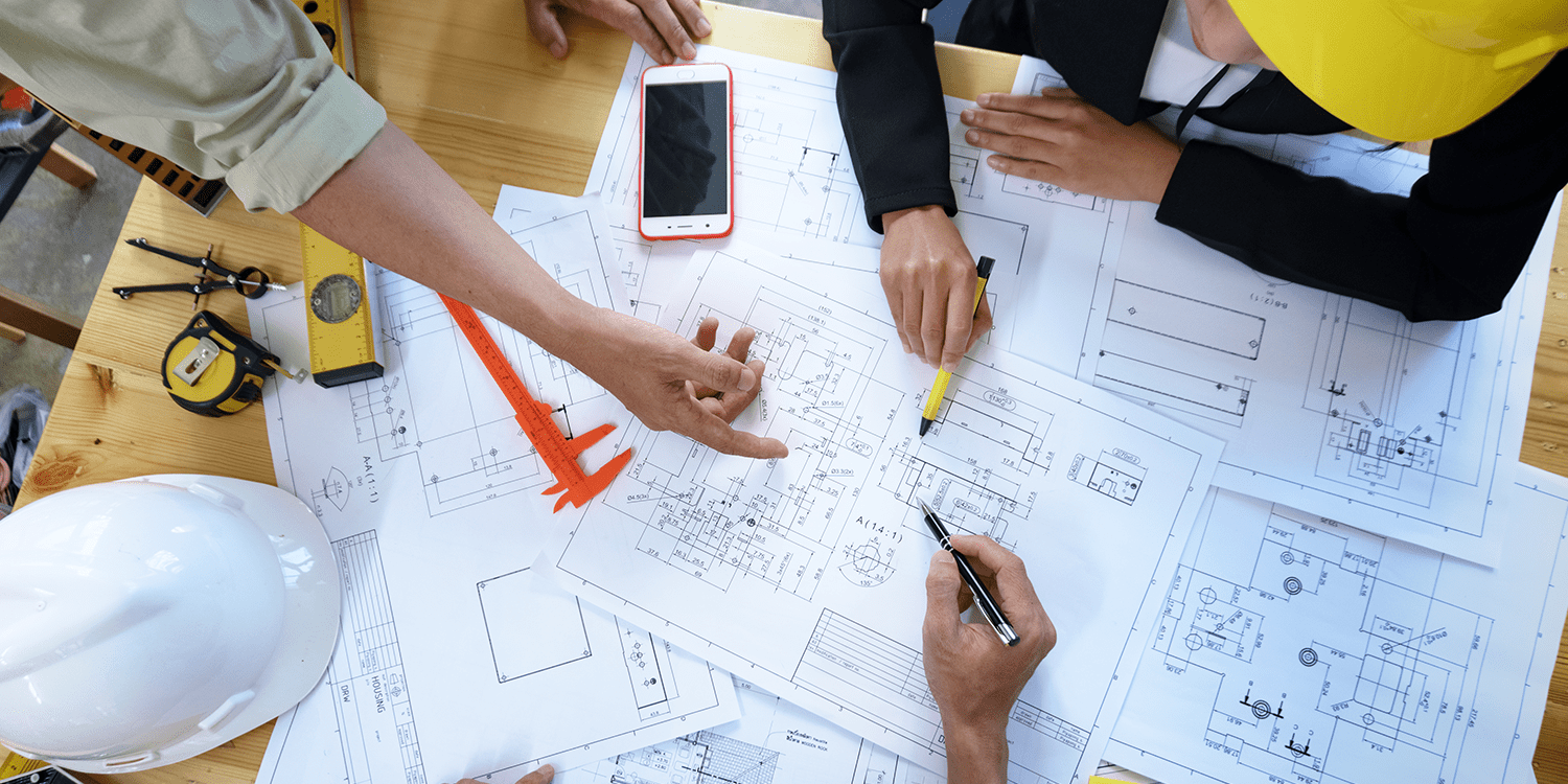 Image of quantity surveyors, who often work as contractors, reading floor plans and blueprints on a large desk