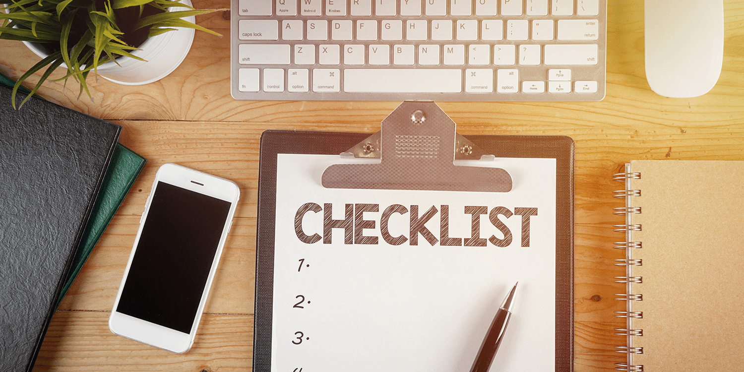 Image of a desk with a keyboard, mobile phone, and a clipboard holding a checklist, illustrating the process creating a business startup checklist.