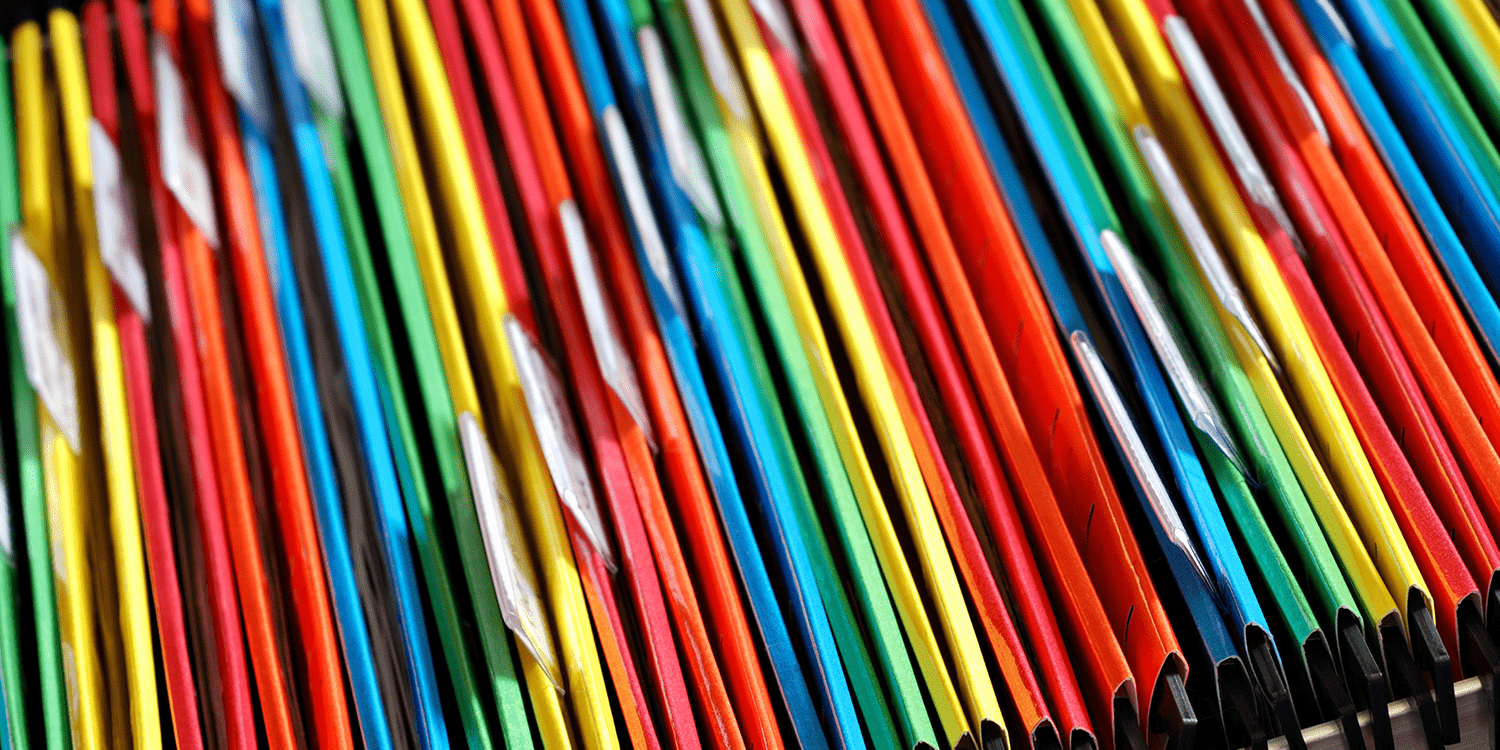 Image of an open drawer of a filing cabinet containing file folders in many different colours, illustrating one way in which company records can be stored.