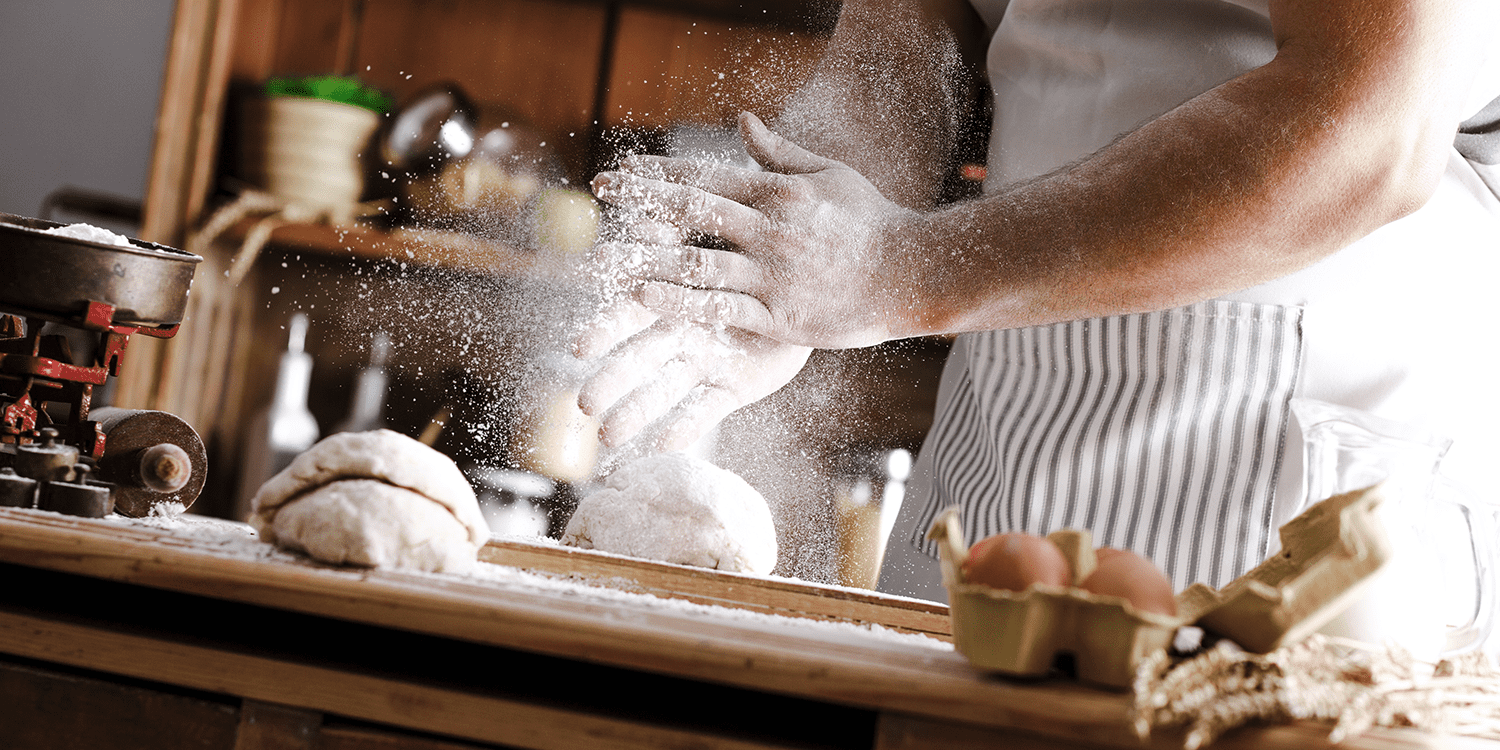 Baker with striped apron making bread in a kitchen on wooden table.