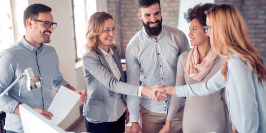 A group of 5 smartly dressed men and women standing together, two of whom are shaking hands.