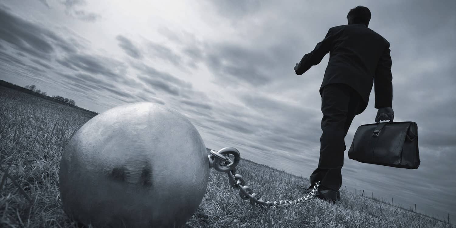 Businessman with briefcase walking with ball and chain attached to his ankle, symbolising the liability of company directors.