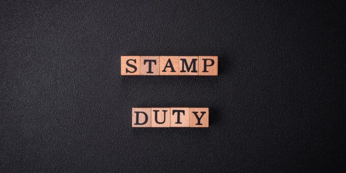 Wooden letter blocks spelling "STAMP DUTY" in two rows, set against a dark textured background.