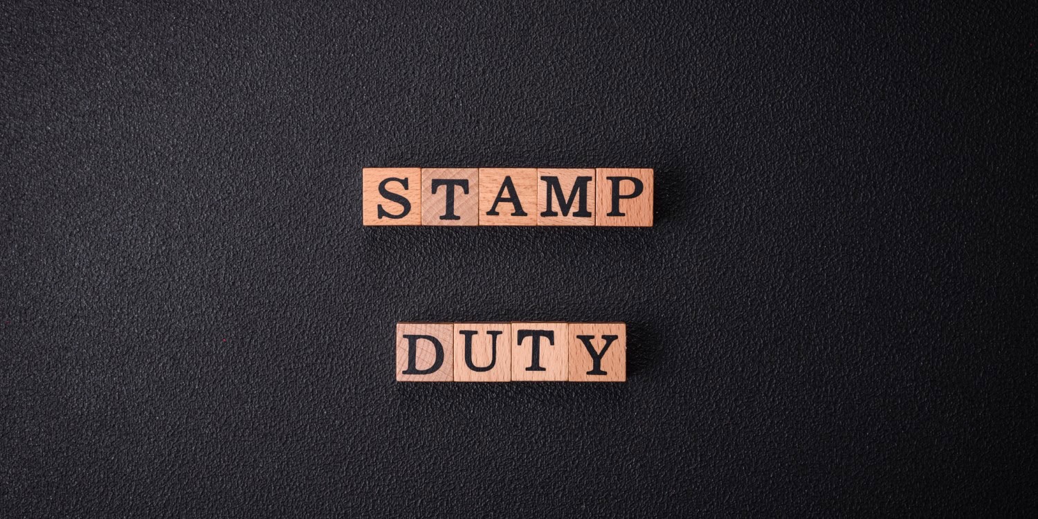 Wooden letter blocks spelling "STAMP DUTY" in two rows, set against a dark textured background.