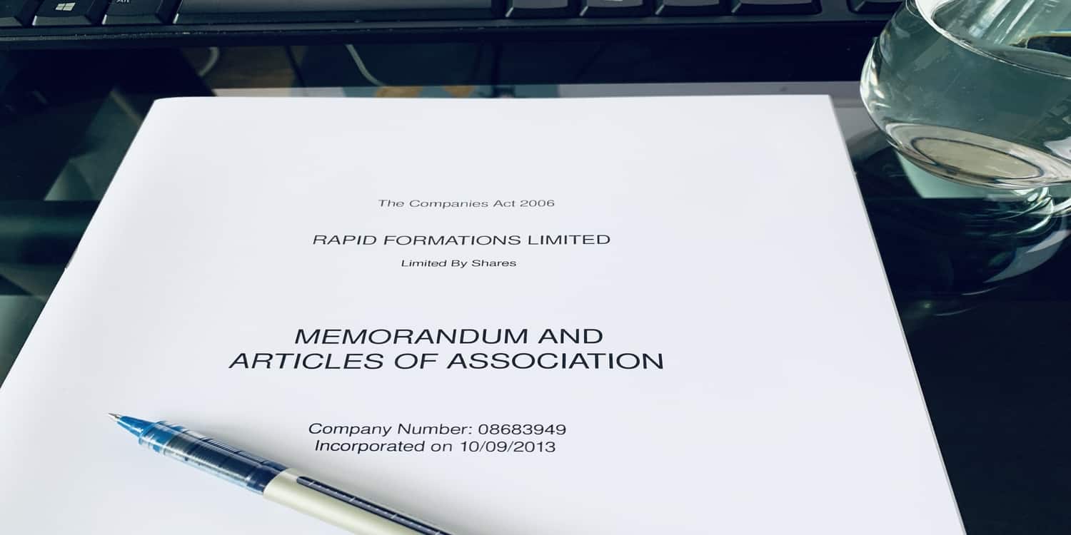 Photograph of memorandum and articles of association on desk with pen and glass of water.