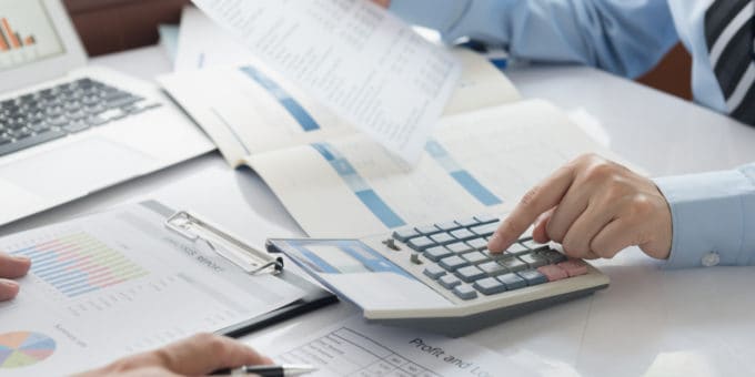 Business person working with a calculator with annual accounts documents on desktop.