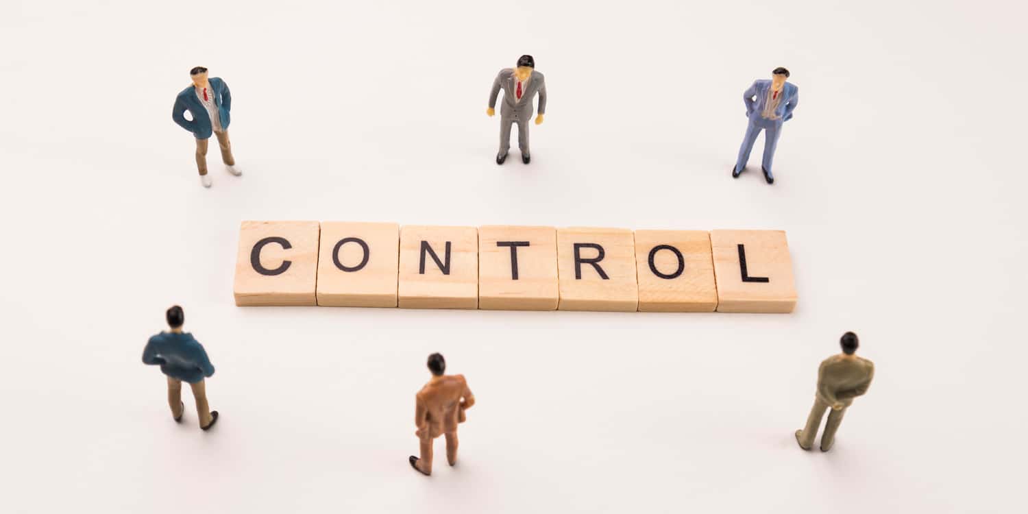 Miniature businessmen standing around wooden blocks spelling the word 'CONTROL.'