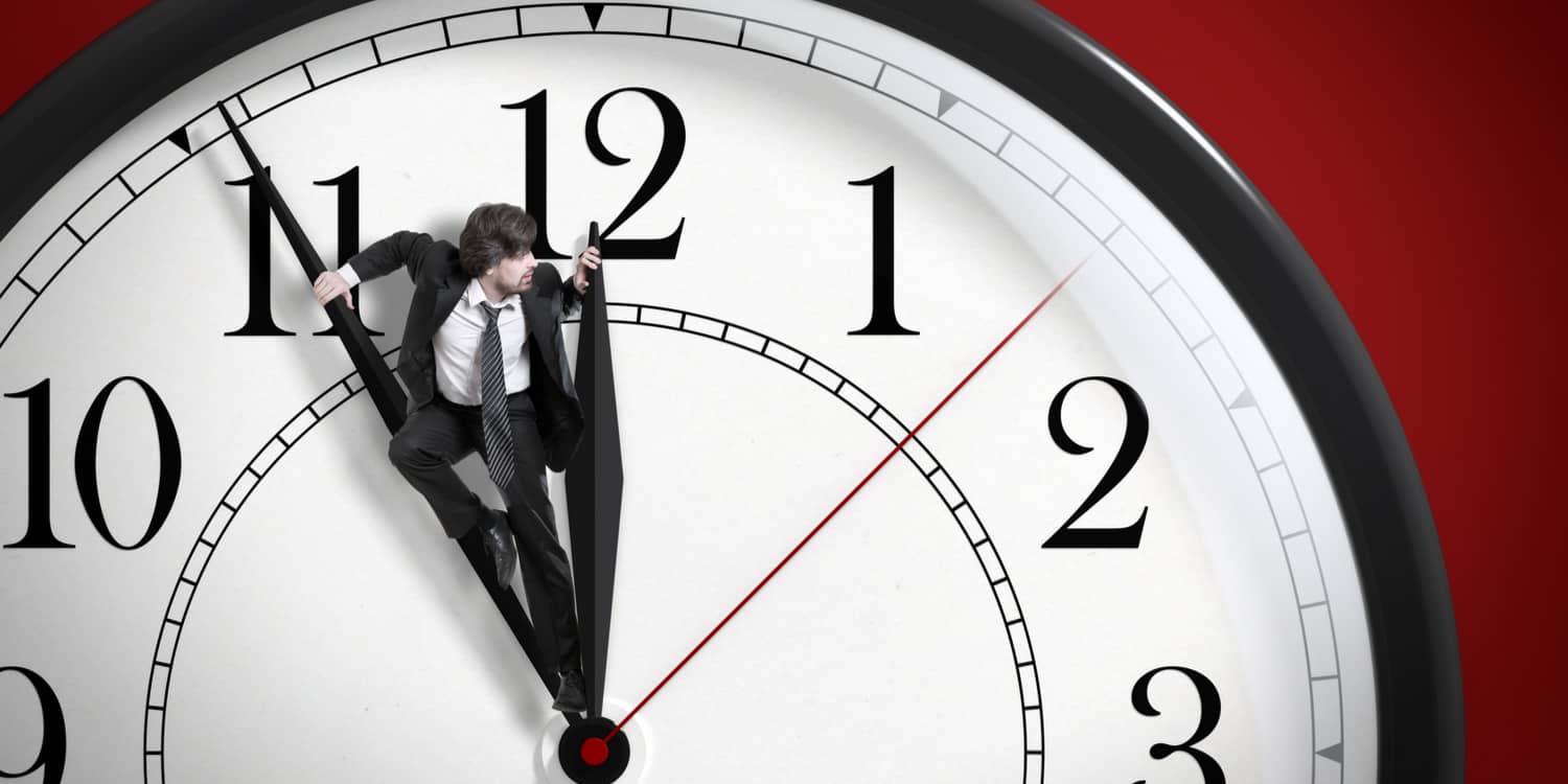 Business man standing on the hands of a clock trying to stop time.