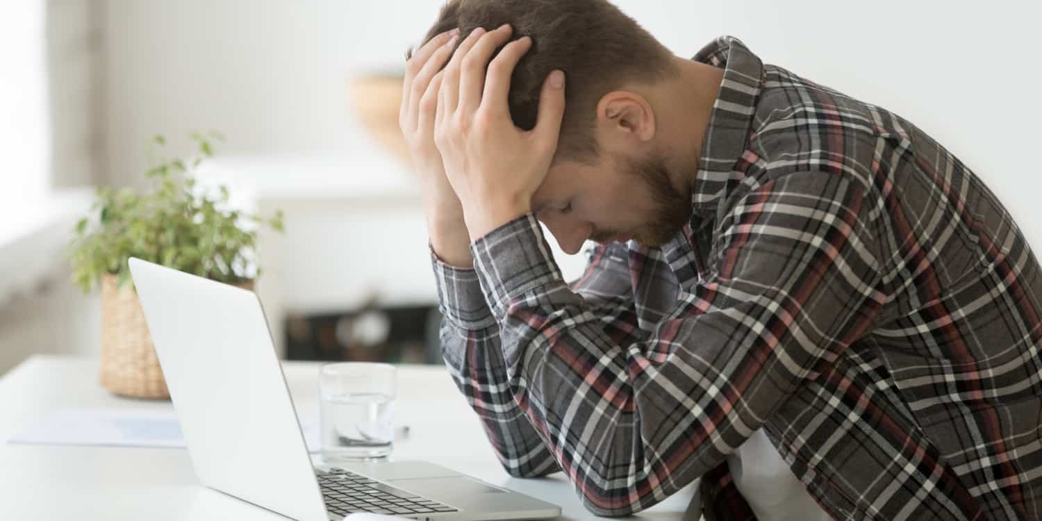 Young man with beard and checked shirt, sitting at laptop with head in hands, having lost his company's WebFiling authentication code.