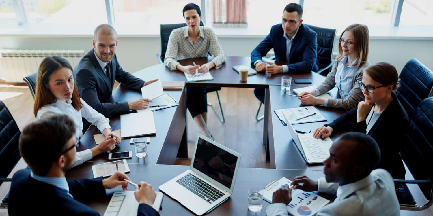 Photo of 8 business men and women sitting around an oval table, illustrating a meeting of limited company shareholders.