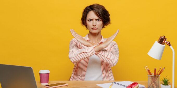 Woman sitting at a desk with a serious expression, crossing her arms in an X gesture, conveying a strong message of “no” to needing an accountant to set up a limited company