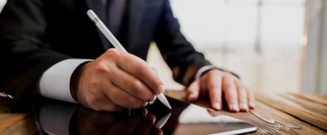 Businessman sitting at desk signing a document on an iPad using a light pen - illustrating the electronic signature concept.