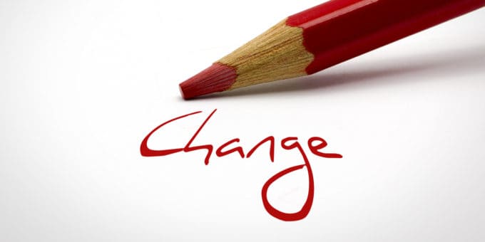 The word 'Change' written in red on white paper with red pencil in background.