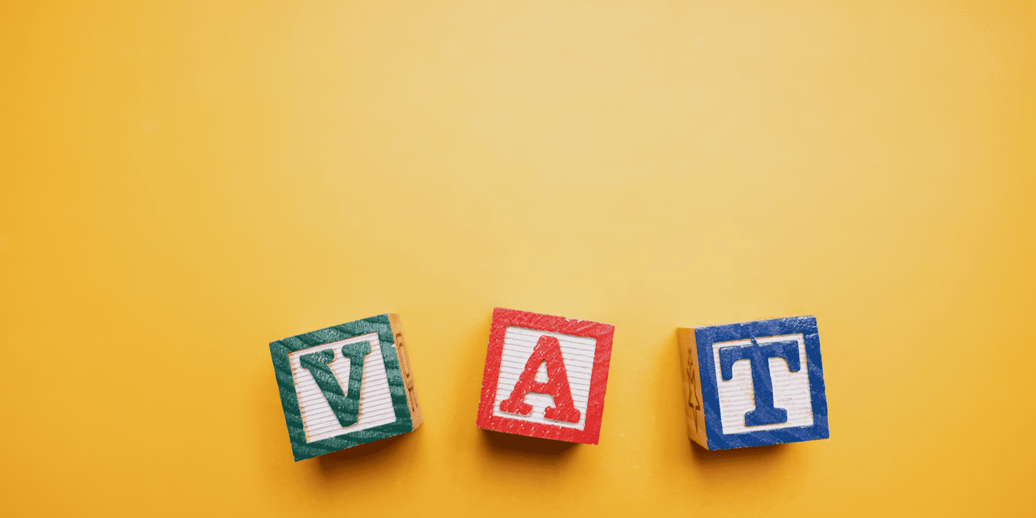 Three colourful wooden blocks spelling the word VAT against an orange background.