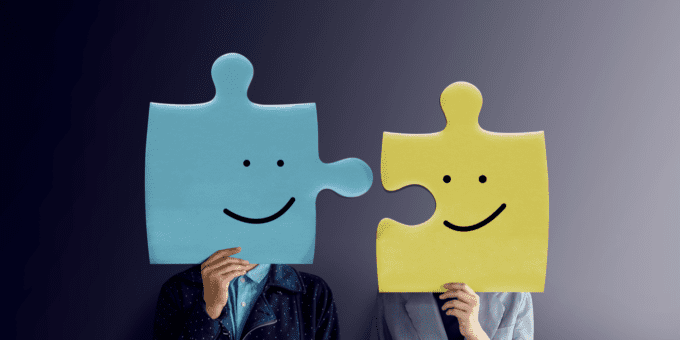 Portrait of two people with happy face emotion on jigsaw puzzles, illustrating the business partnership concept.