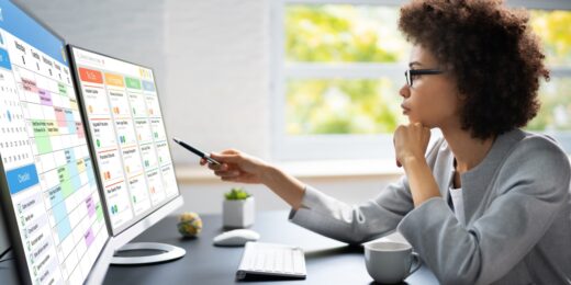 A woman looking at two computer screens, which display to-do lists and project management tools.