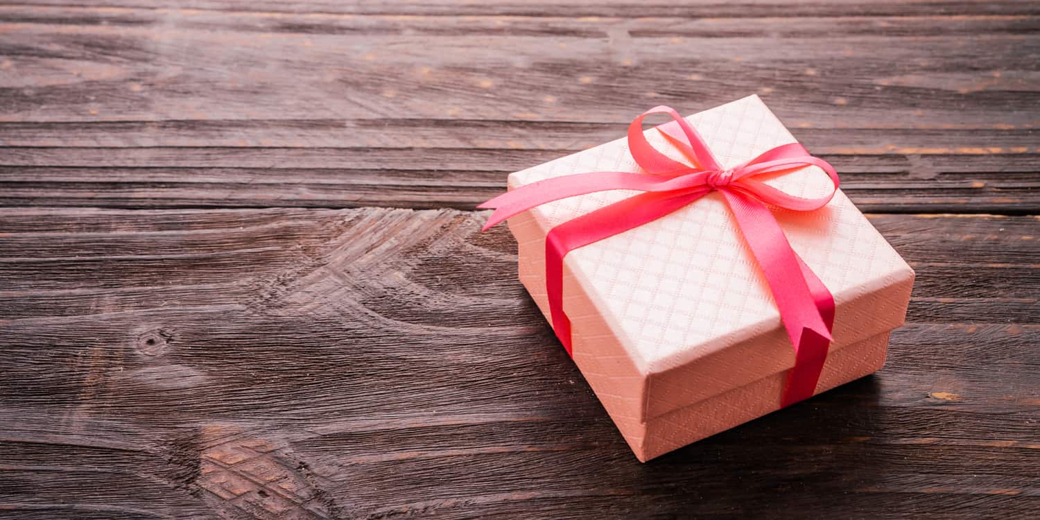 Pink gift box with red ribbon on wood background.