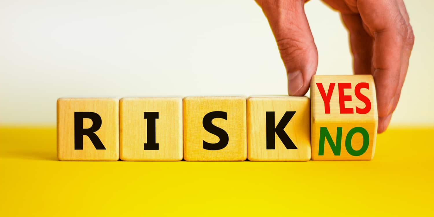 A hand turns a wooden cube and changes words 'risk yes' to 'risk no'. On yellow table with white background,
