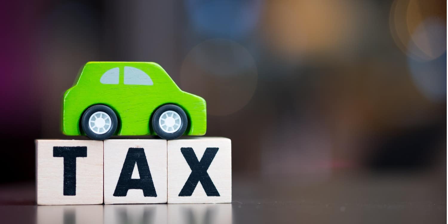 Wooden toy car sitting on top of wood cubes with word TAX.