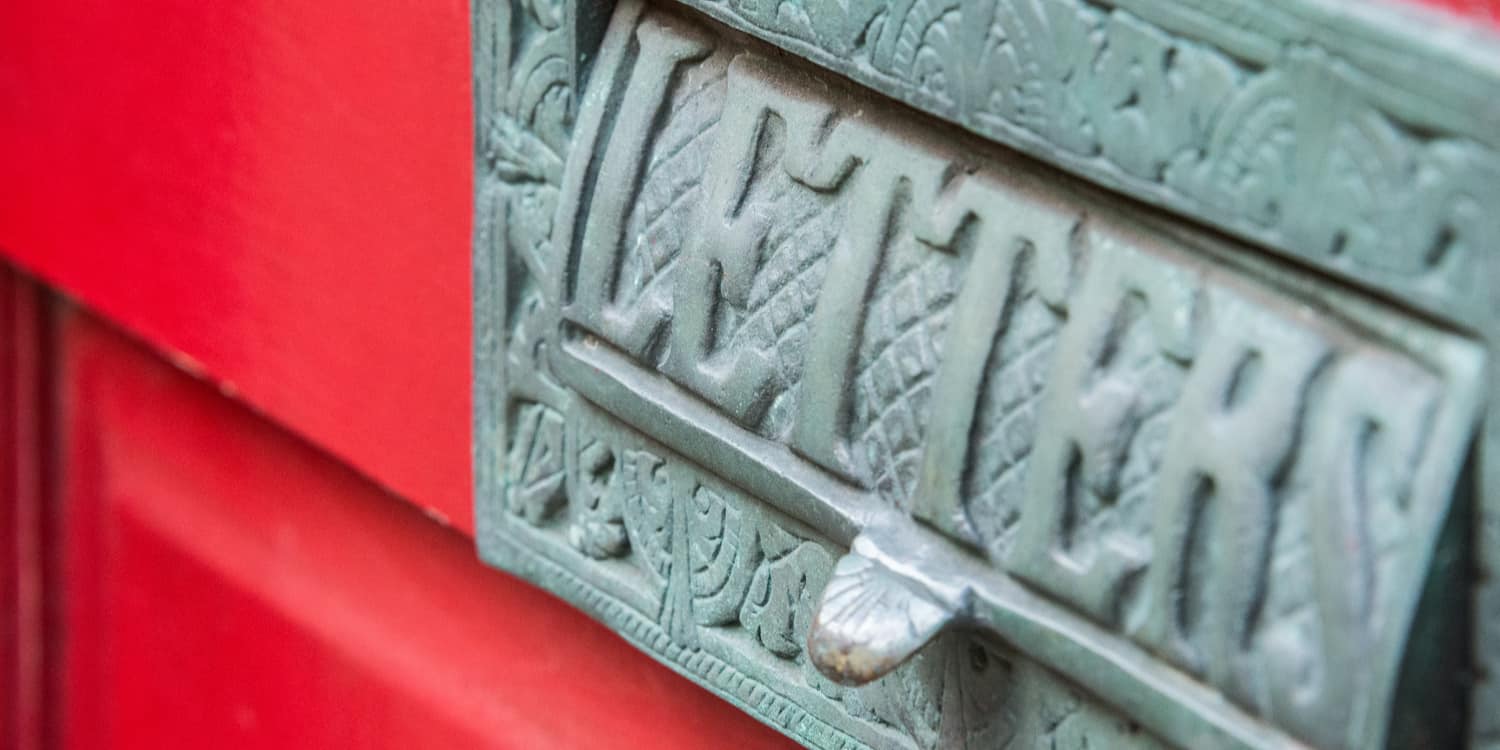 A brass letter box inscribed with "Letters" and other patterns tarnished green on a red wooden door.