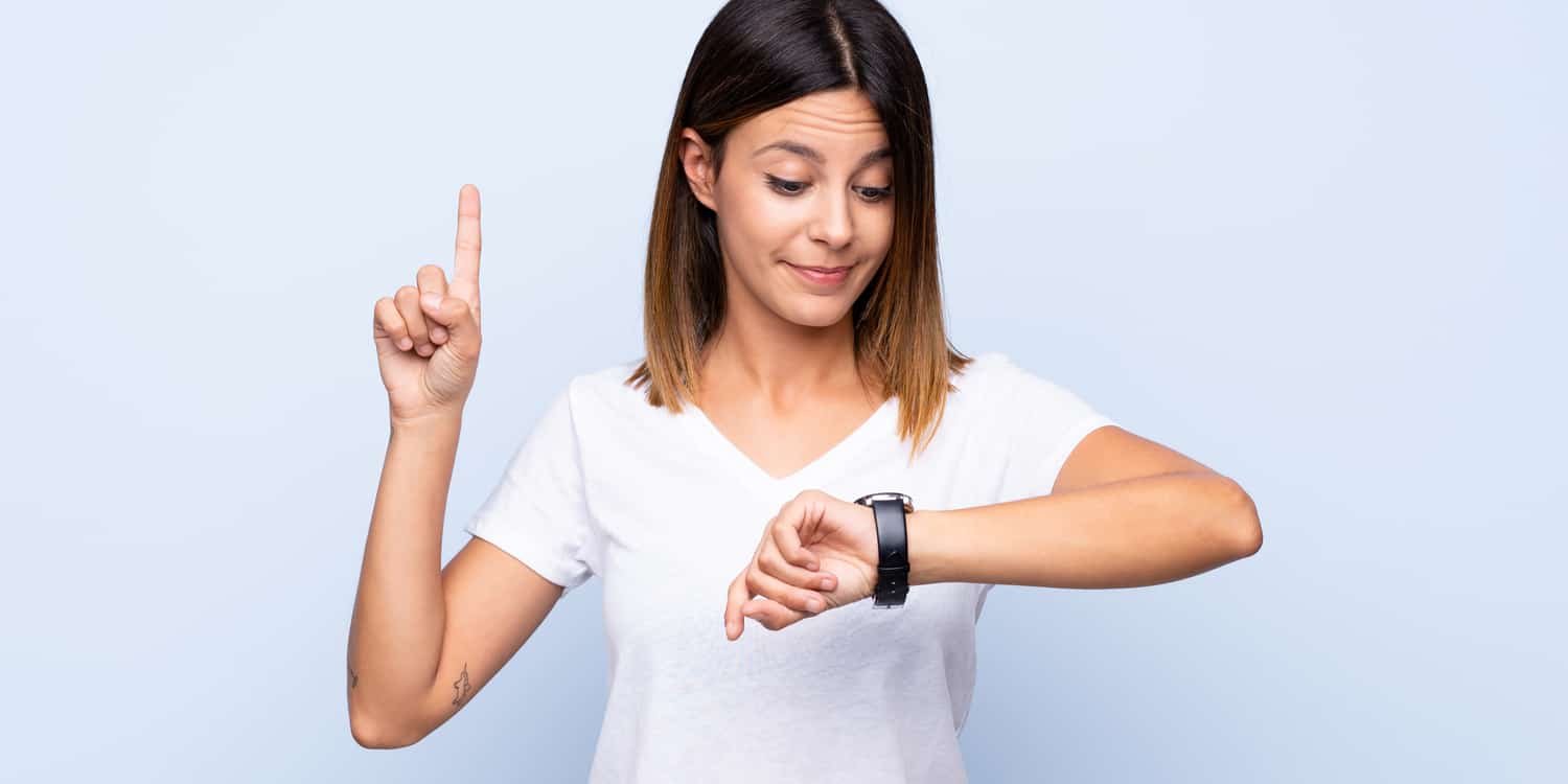 Young woman looking at her watch with the index finger of her other hand raise in the air .