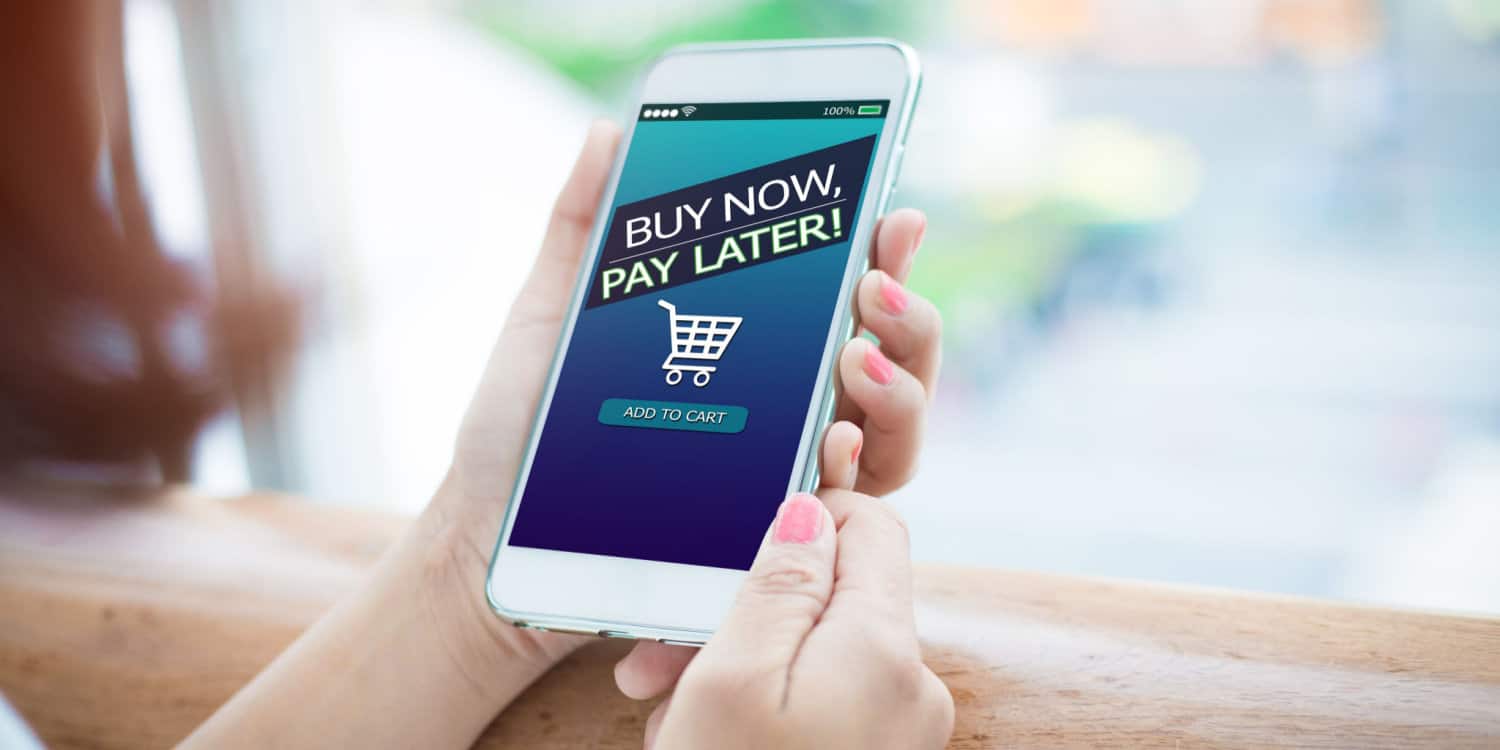 Hands holding mobile phone with Buy Now Pay Later shopping cart displayed on screen.