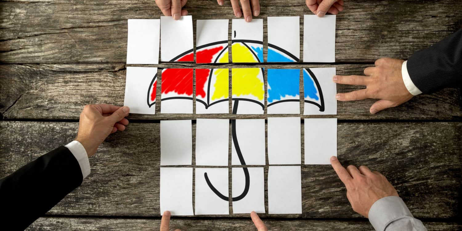 Top view of eight male hands assembling a colourful umbrella with cards over textured rustic desk. Conceptual of umbrella company.