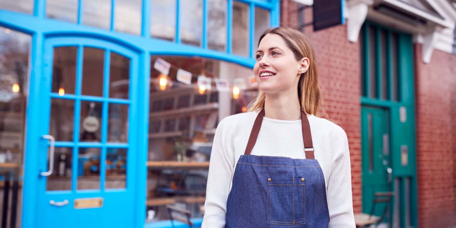 Image of a smiling female business owner standing outside her principal place of business.