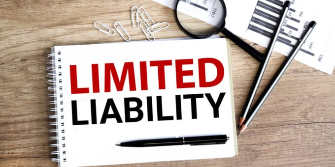LIMITED LIABILITY printed on a notepad lying on a wooden desk with pen and pencils beside it.