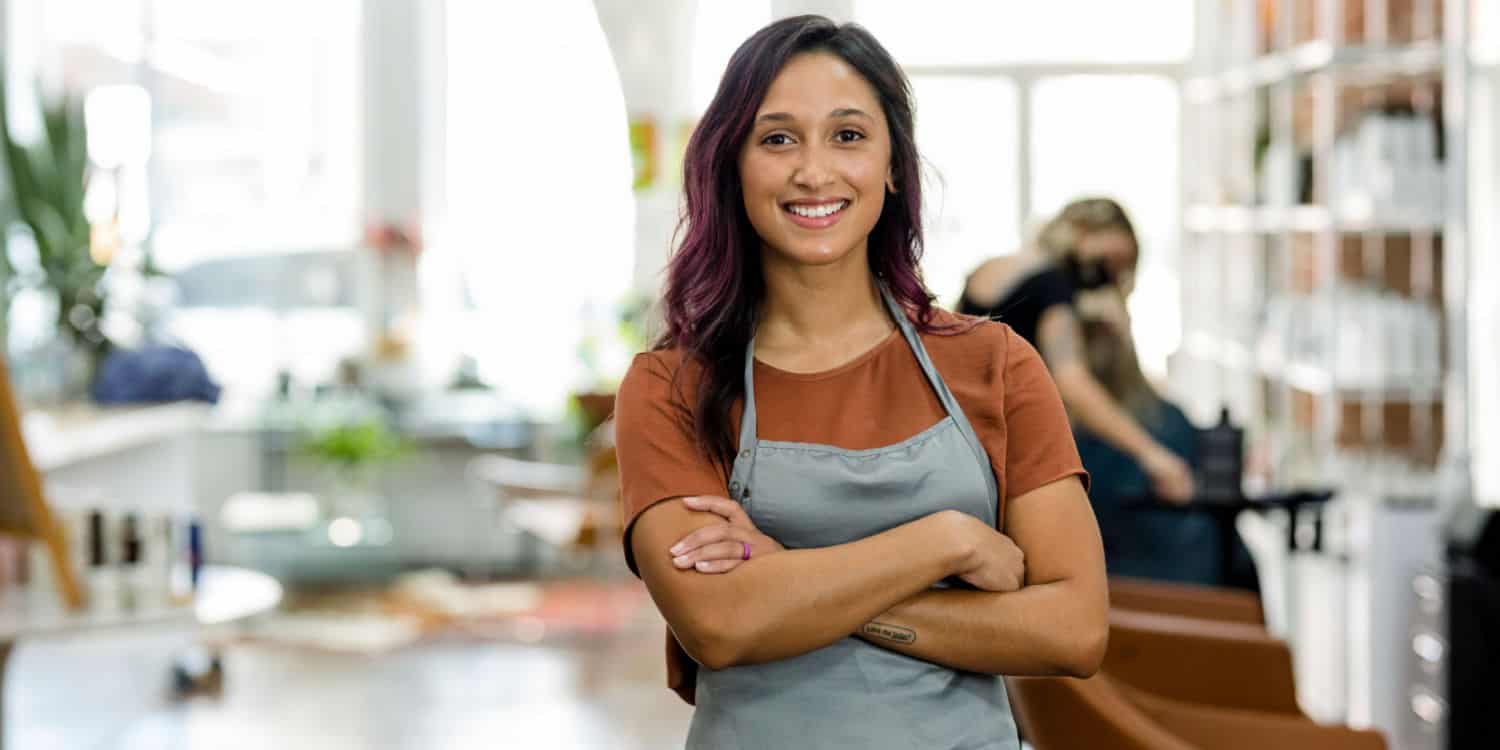 A smiling female business owner standing in her beauty salon wearing an apron.