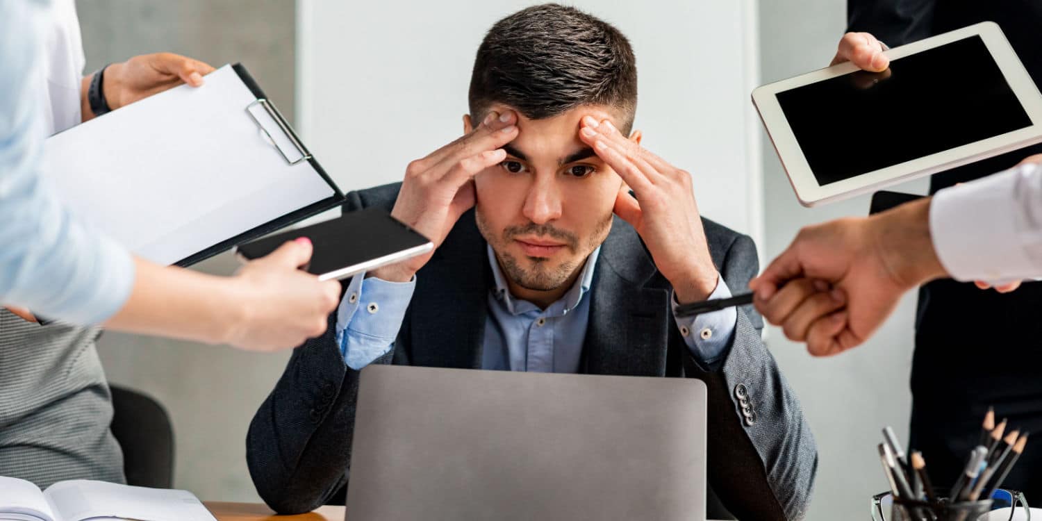 Stressed businessman sitting at office desk being inundated with tasks to perform from other colleagues, demonstrating the concept of running multiple businesses.