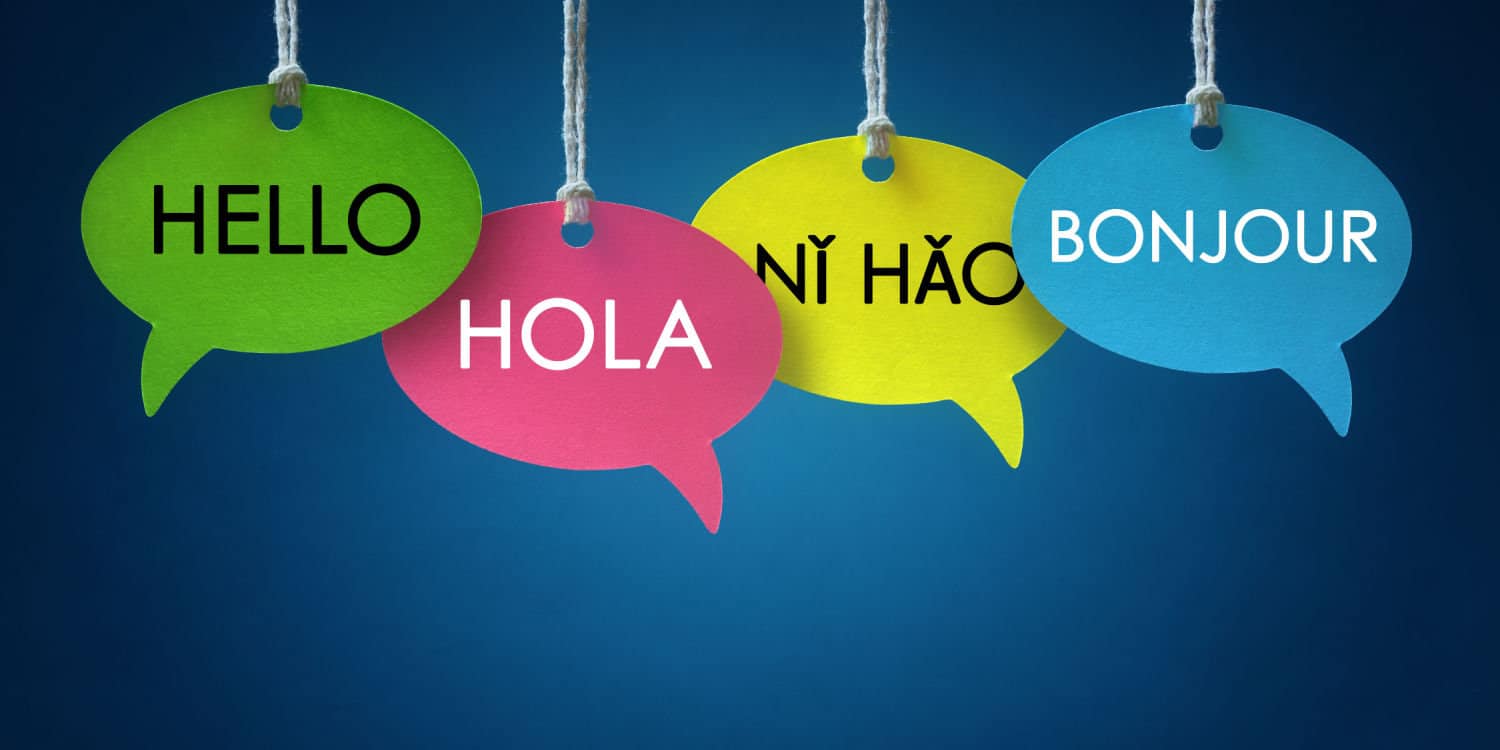 Greetings in different languages displayed on colourful speech bubbles hanging from a cord over a blue background.