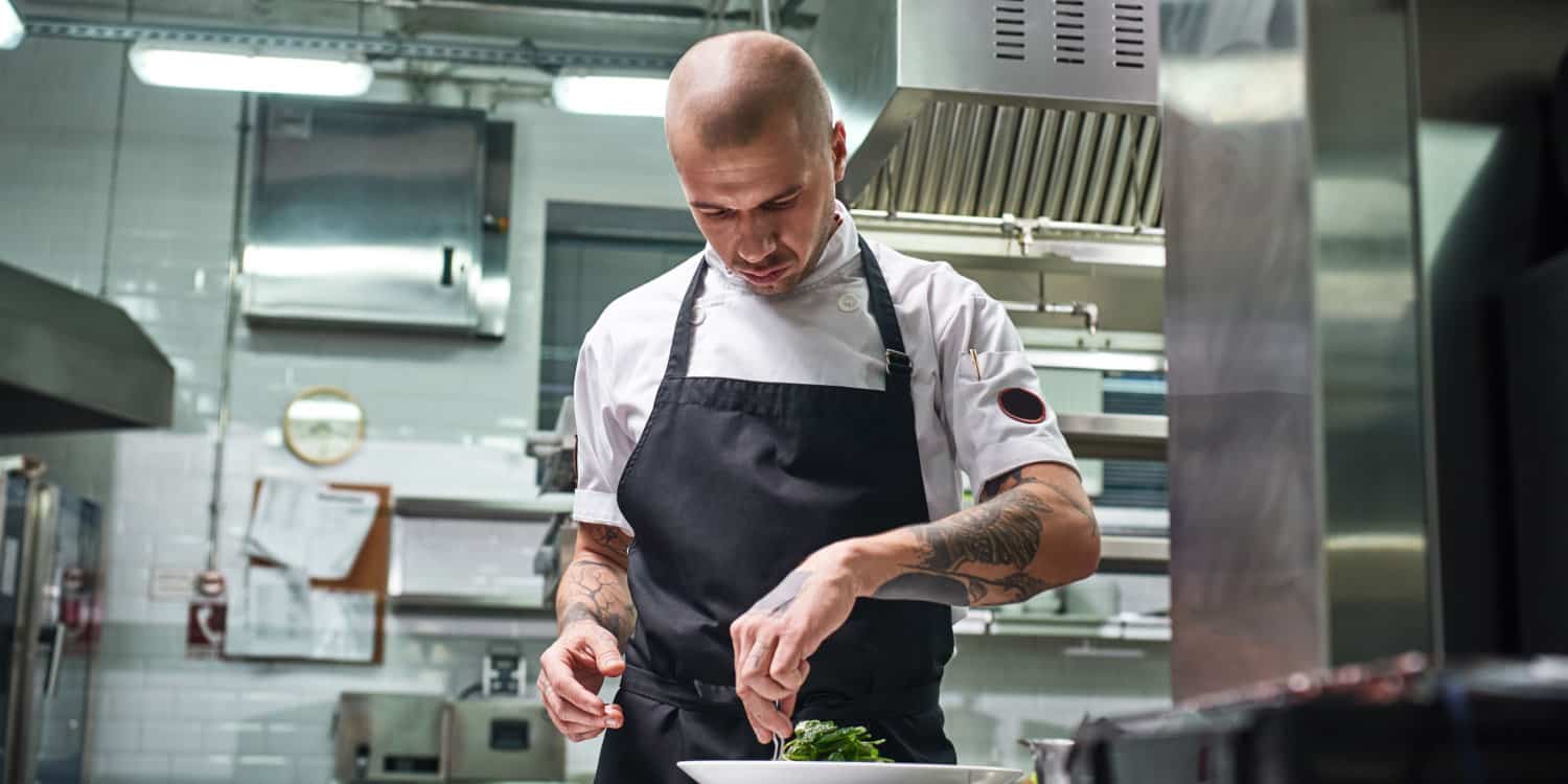 Young ex-offender with tattoos on arms working as a chef in a commercial kitchen.