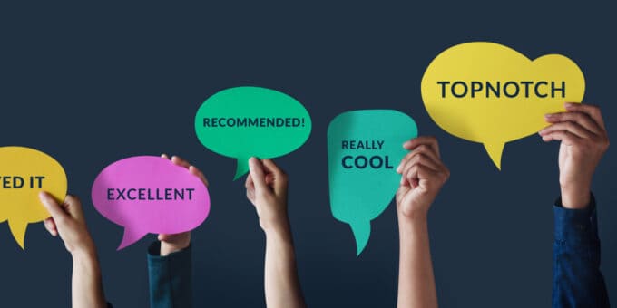 Group of hands holding up cardboard speech bubble cards with positive statements about a business including 'Excellent', Recommended' and Really Cool'.