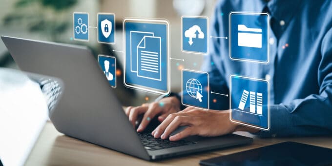 Businessman using a laptop to store company records with icon imagery of the different methods of storage, e.g. cloud, PC document files, etc.