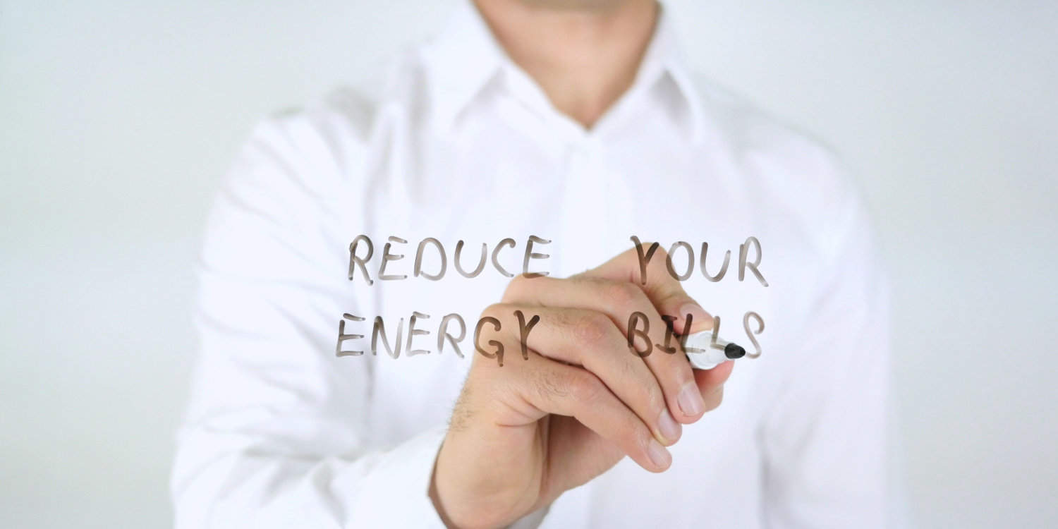 Businessman in white shirt writing 'REDUCE YOUR ENERGY BILLS' on glass.