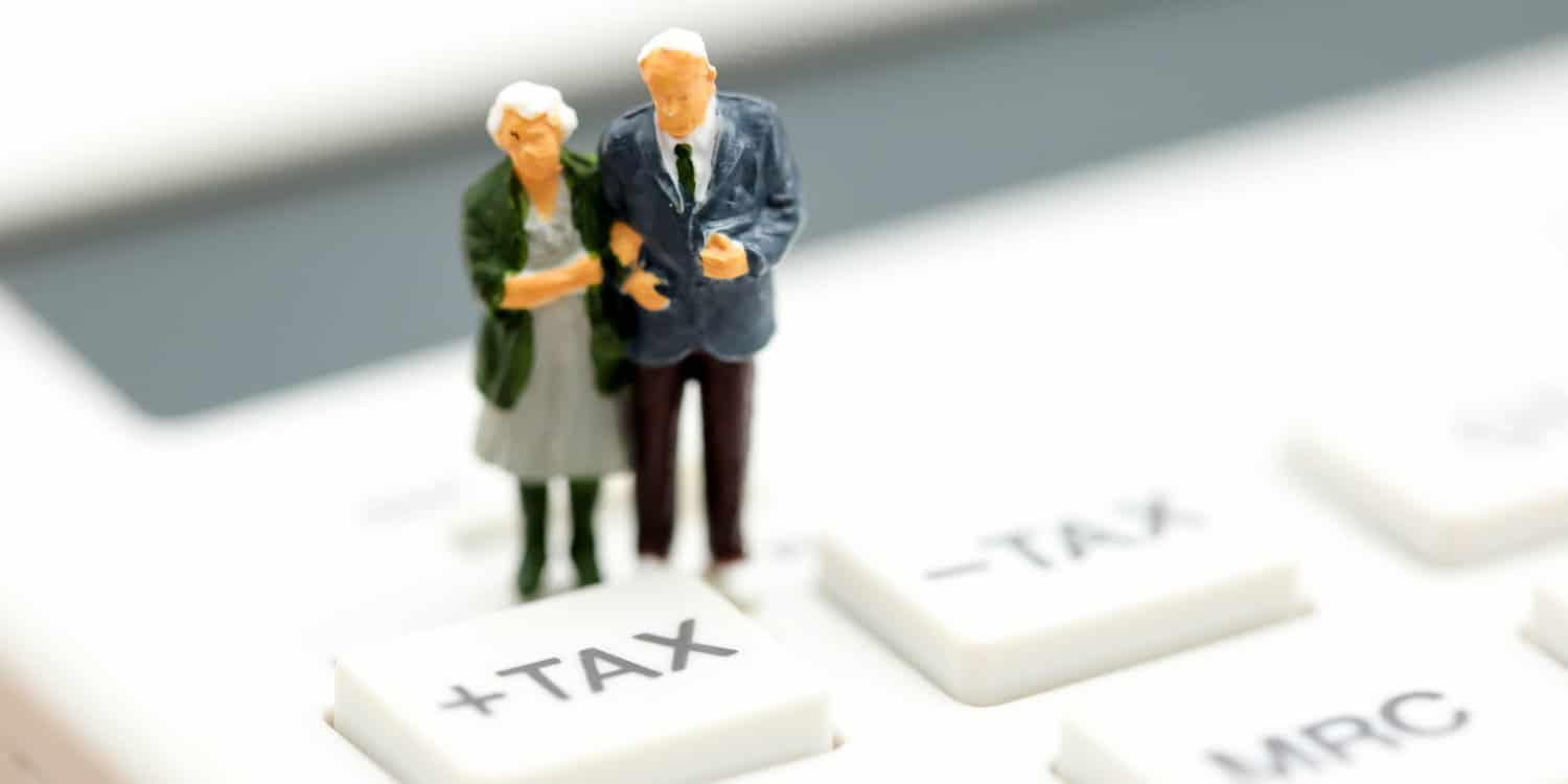 Miniature old couple standing on a pocket calculator beside the keys '+TAX' and '-TAX' illustrating the concept of Inheritance Tax.