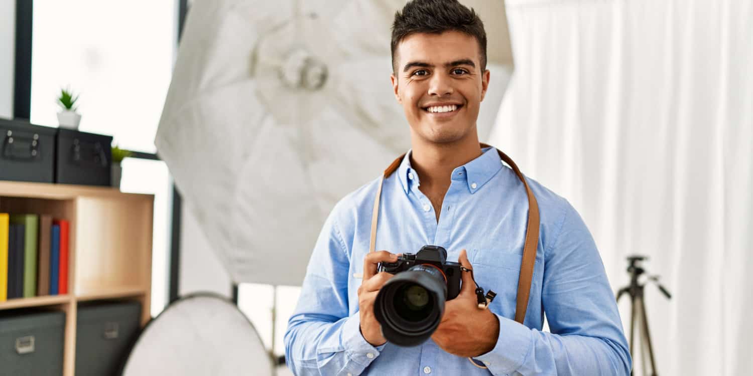 Young owner of a photography business holding a professional camera at his photography studio