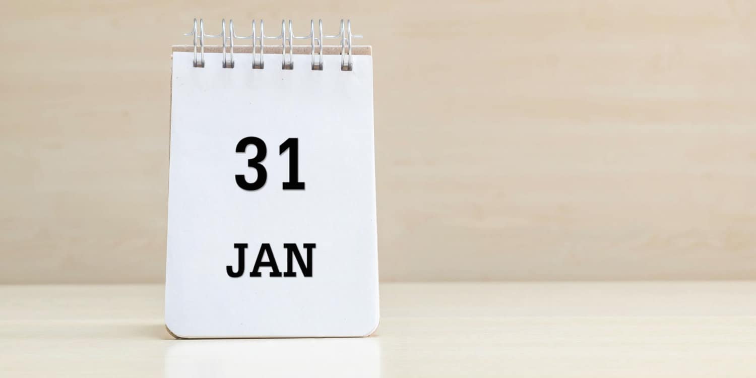 Closeup of notebook standing on wooden table '31 JAN' displayed in black letters, with headline of 'DEADLINE for online tax returns' in red letters.