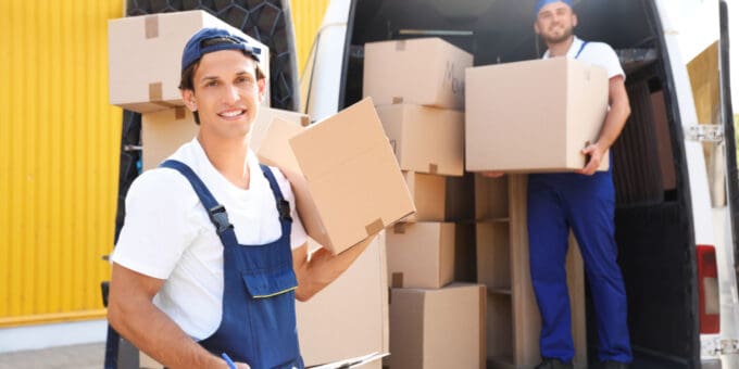 Removal company owner unloading a van if cardboard boxes with assistant in the background.