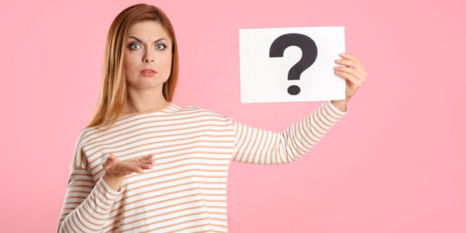 Confused woman holding up a question mark sign on pink background.