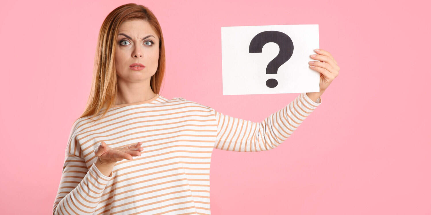 Confused woman holding up a question mark sign on pink background.